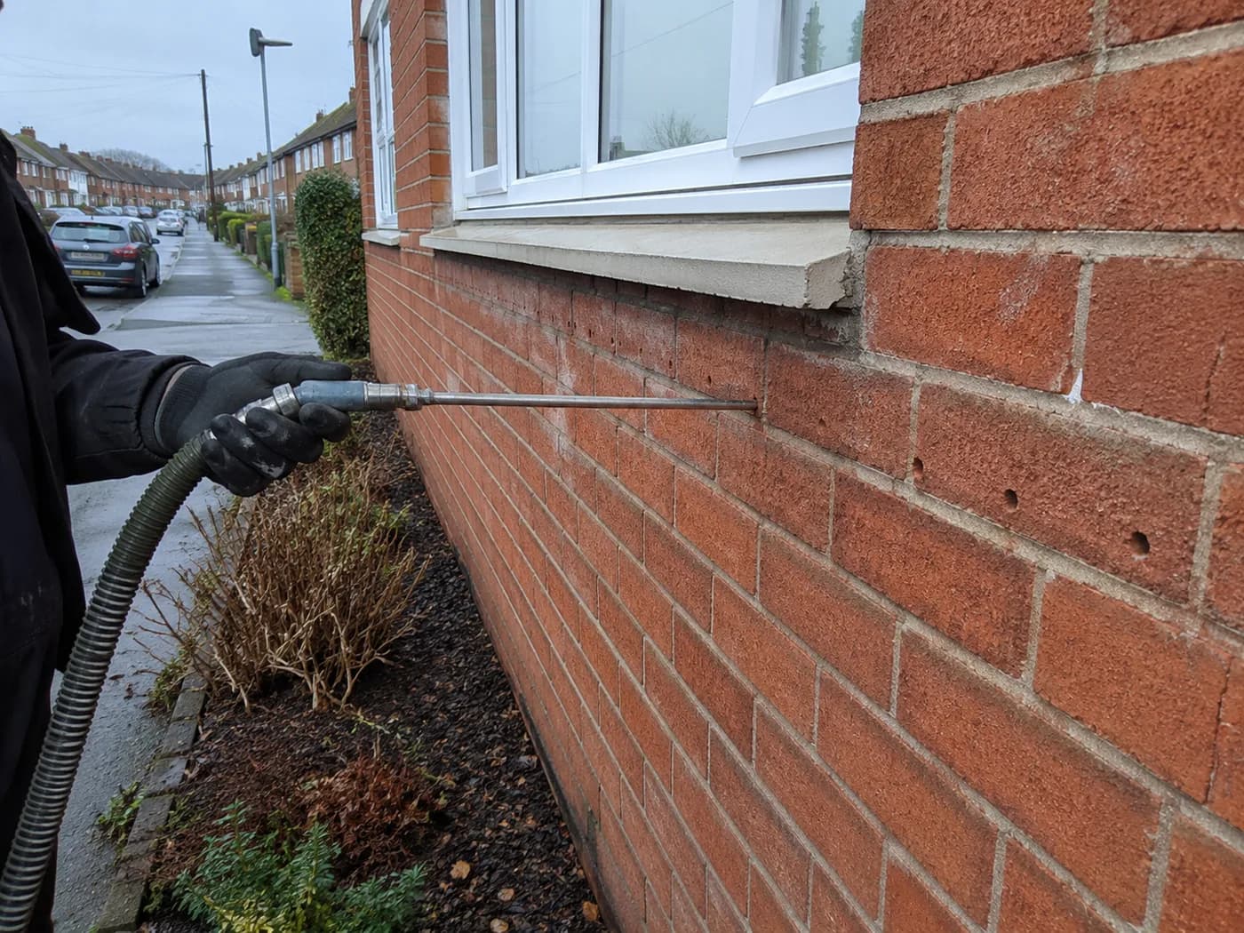 An installer injecting bead insulation into a drilled hole in a brick cavity wall